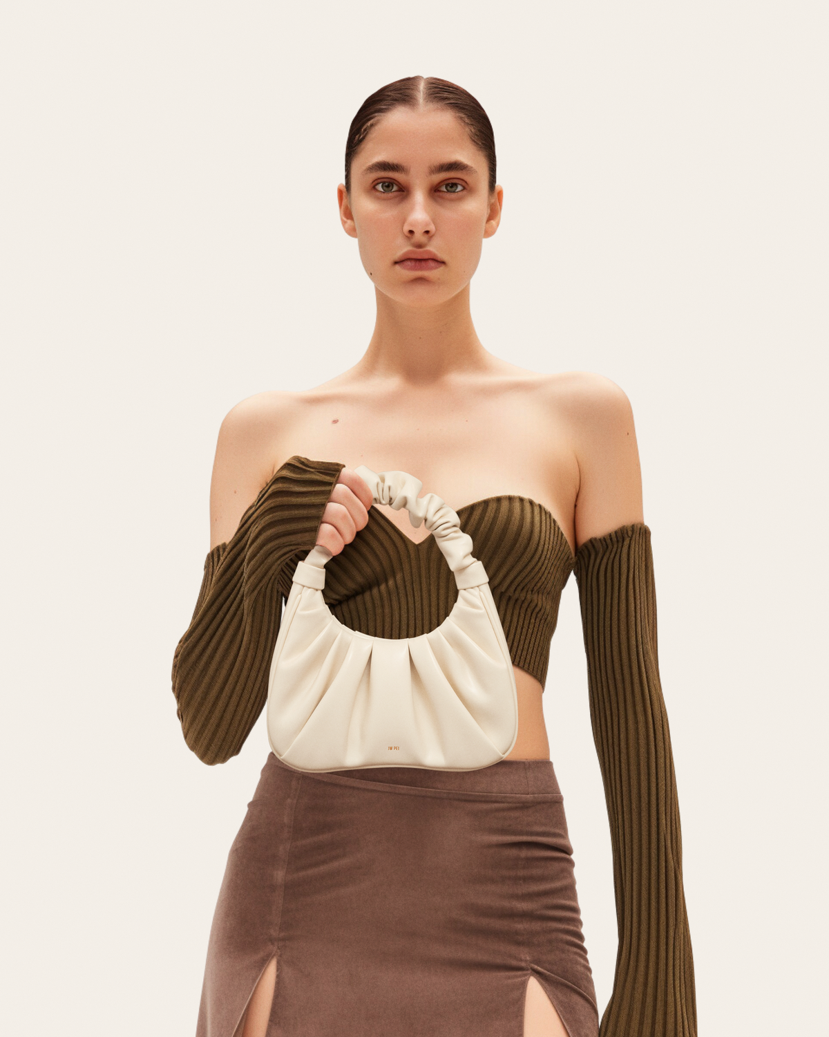 Woman holding a beige handbag against a plain background